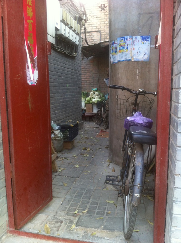 Entrada de um siheyuan (grupo de casas) mostra uma bicicleta encostada e o armazenamento de repolhos, bastante comum no inverno