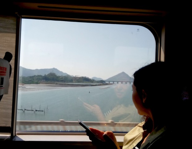 Vista do trem na província de Guangdong mostra uma passageira olhando para o mar